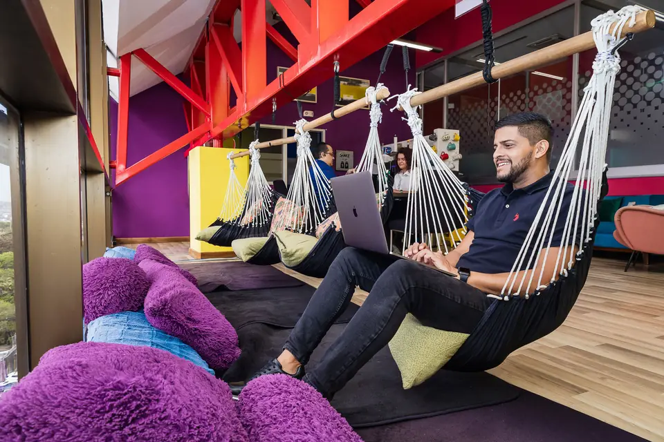 An IDEACTIVO team member works on a laptop from a hammock in a colorful office