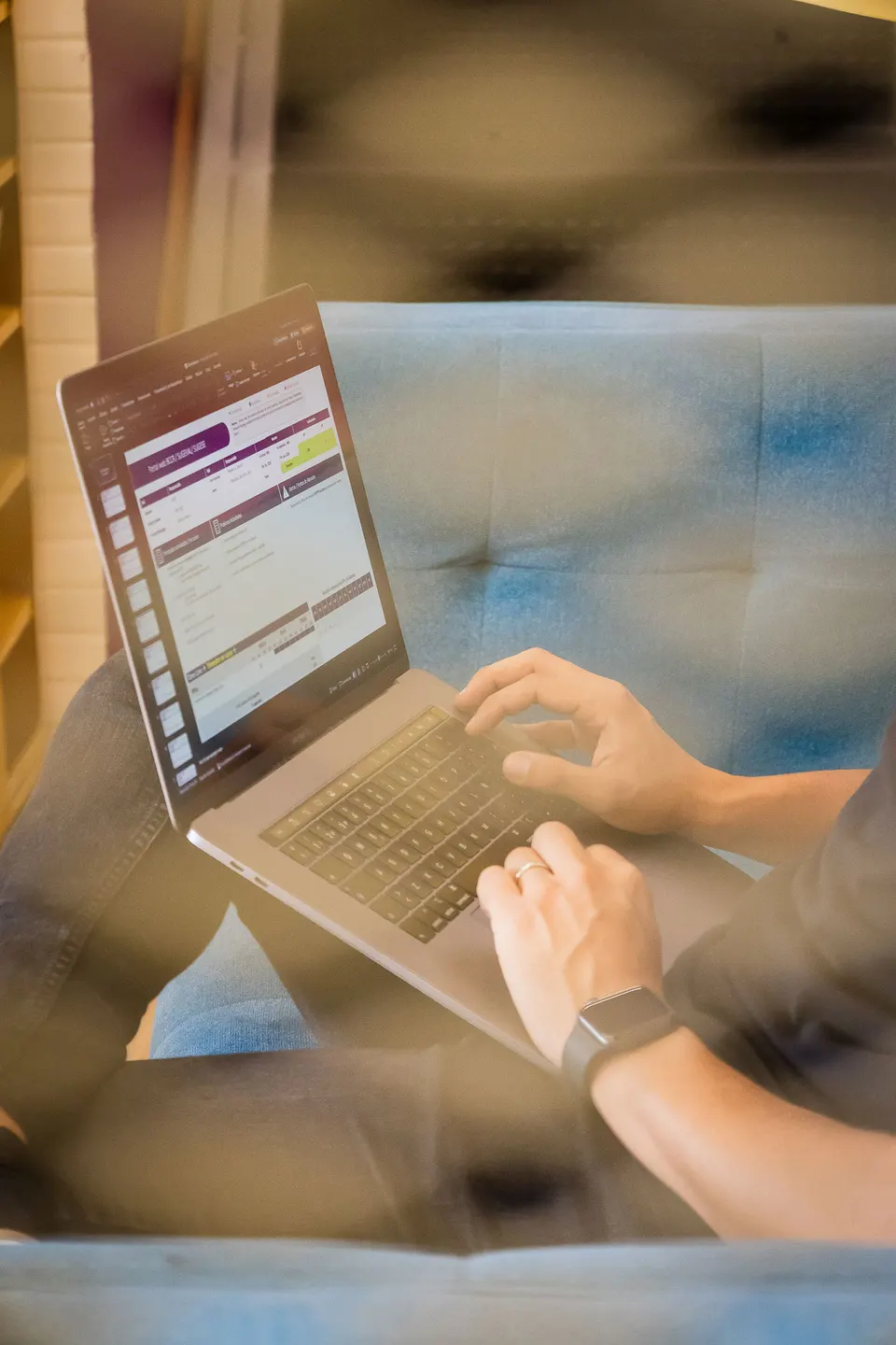 Person on an armchair reviewing a project status report on a laptop